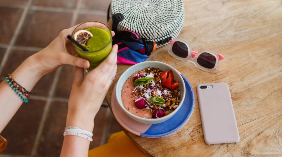 Woman holding smoothie. Superfoods  bowl topped with chia, granola and avocado. Overhead, top view, flat lay. Healthy breakfast. Summer accessories.